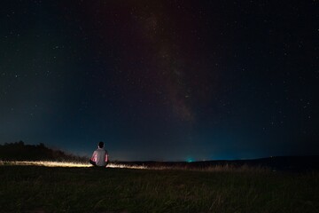 Beautiful night sky with stars and silhouette of a standing alone man on the mountain with a lantern. Blue milky way and man on the hill. Background with galaxy and silhouette of a man. 