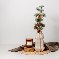 Winter interior, vase with fir tree and candle in a glass jar with brown towel at the background. Holidays cozy home decoration, scandinavian style