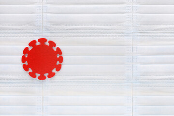 Coronavirus molecule cut out of red felt on light blue medical masks background. World wide...