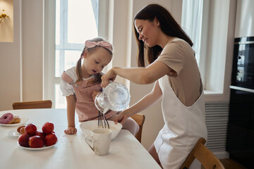 An image of a young woman and her little cute daughter are cooking in the kitchen. Have fun...