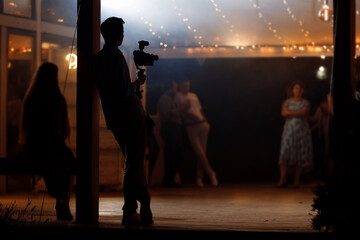 Silhouette of cameraman standing with video action film production digital camera at wedding, birthday party. Professional videographer is working, shooting and filming in the event.