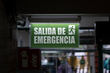 Lit up sign in Spanish emergency exit next to an open door. Safety, danger, natural disaster concept.