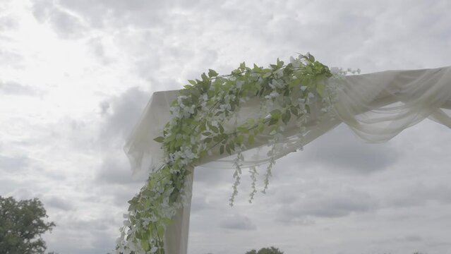 A wedding Chuppah, Mandap, Arbor, Canopy with greenery and white sheer fabric for a religious outdoor wedding on a golf course.