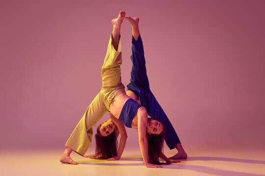 Energetic dancers in art performance at dance hall. Young stylish fashionable girls dancing isolated on crystal pink background. Art, fashion, style
