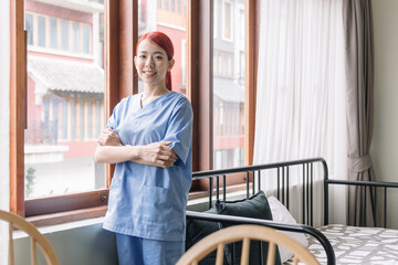 Fototapeta premium Portrait of Asian therapist woman nurse wearing medical scrubs in the house of patient. Caregiver visit at home. Home health care and nursing home concept.