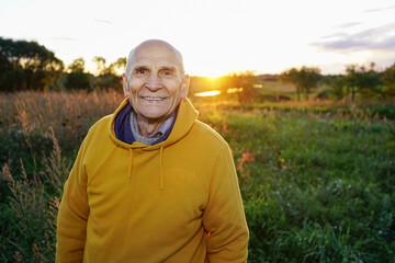Naklejka na ściany i meble Elder man wearing yellow hoodie posing to camera outdoor. Portrait of mature happy farmer smiling with teeth.