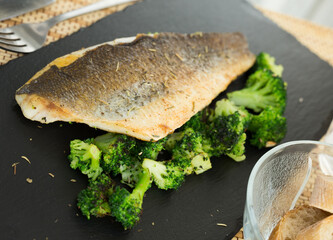 fried fillet of sea bass with garnish of broccoli on black warm stone plate