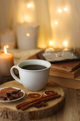 Fototapeta premium Bowl of cookies, cup of tea or coffee, chocolate, spices, knitted blanket, books, glasses and candle on the table. Cozy hygge atmosphere at home. Selective focus.