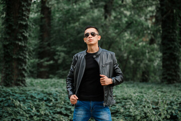 Portrait of a handsome brutal man in a black leather jacket in a forest