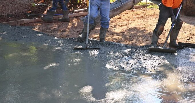 Construction contractors pouring wet concrete while paving driveway as they work on concrete construction project
