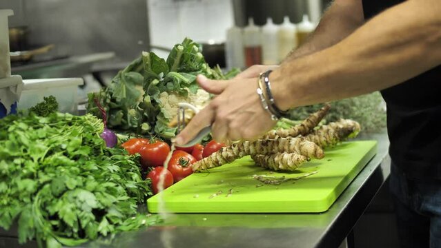 Unrecognizable chef using peeler to peel fresh sunroot in restaurant kitchen, close up