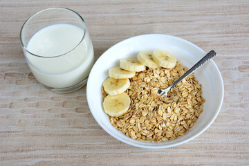 oatmeal flakes in white bowl with banana slices and glass of milk