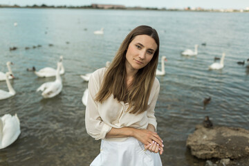 young woman stands next to a beautiful lake and white swans