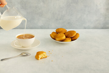 Delicious snack: a cup of black tea with milk and a plate of cookies on a gray background.