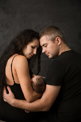 Young parents with their baby on a dark background, back view
