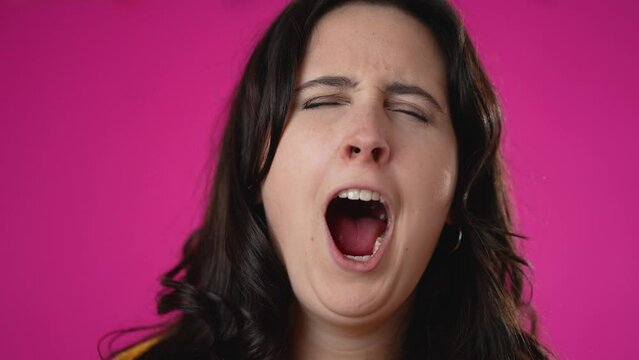 Slow motion pretty brunette young woman 20s 30s did not get enough sleep last night after party and barely got up in the morning yawning. Closeup portrait isolated on pink background in studio.