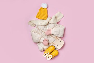Kids warm puffer jacket with yellow  hat and boots on pink background. Stylish childrens outerwear....