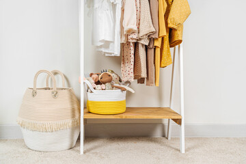 Clothing Rack with children's autumn outfit and Storage Baskets. Yellow, beige, white jacket, dress and sweaters on hangers in wardrobe. Nursery Storage Ideas. Home kids wardrobe.