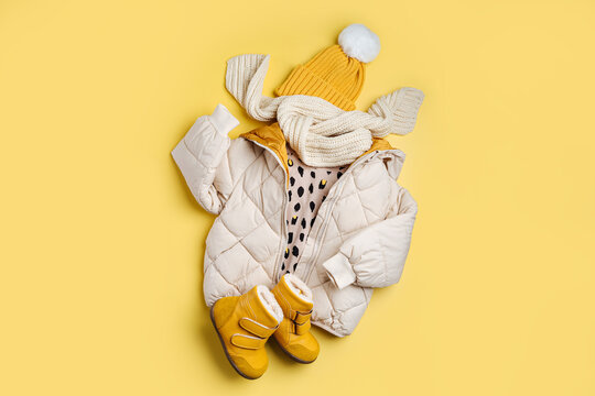 Kids warm puffer jacket with hat and boots on yellow  background. Stylish childrens outerwear. Winter fashion outfit