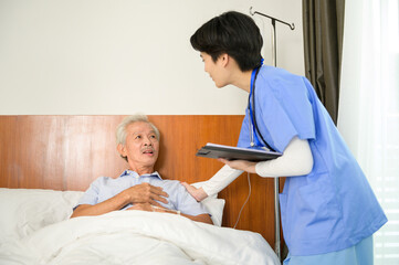 Asian nurse taking care of an elderly man lying on patient bed at  senior healthcare center.