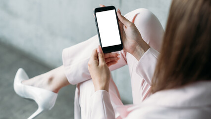 Online project. Digital mockup. Mobile technology. Elegant confident lady holding smartphone blank screen sitting chair in light room interior.