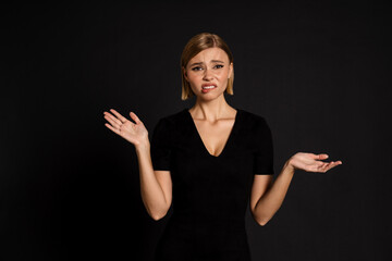 Confused woman holding copyspace on two palms isolated over black background