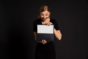 Amazed woman opening black gift box isolated over black background