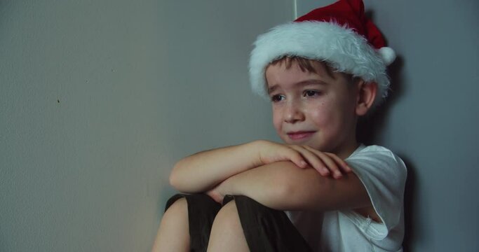 Portrait Cute boy in Christmas Hat Santa Clausa with big tears running down his cheeks, child sitting in corner lifestyle,tears are flowing with a screaming face. Child Sad