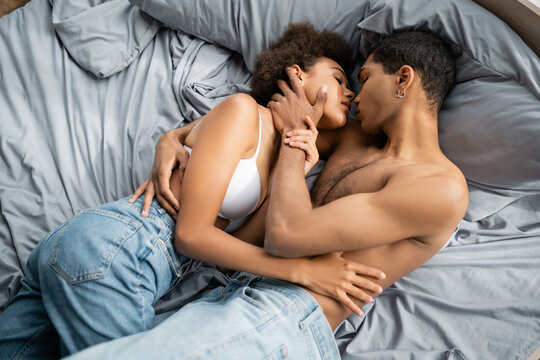 top view of shirtless african american man hugging hot woman in jeans and bra on bed.
