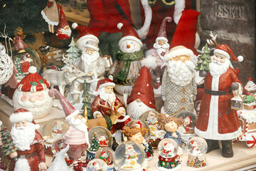 Stylish Christmas souvenirs, santa clauses, snow globes, snowman toys in showcase of festive store. Modern christmas decor in city street. Winter holidays in Europe. Merry Christmas