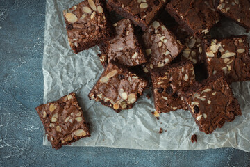 Delicious homemade chocolate brownies with almond flakes and raisins cut on square slices on the baking parchment. Flat lay. Grey concrete background