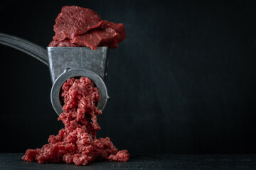 Making minced meat for beef meatballs in a manual meat grinder on a black background. Macro shot....