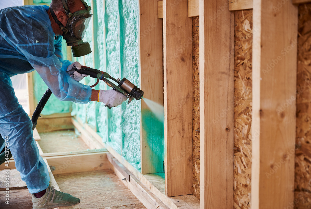 Wall mural male builder insulating wooden frame house. man worker spraying polyurethane foam inside of future c