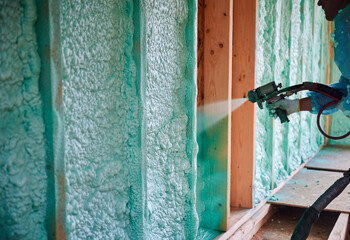 Builder insulating wooden frame house. Close up view of man worker spraying polyurethane foam inside of future cottage, using plural component gun. Construction and insulation concept. - obrazy, fototapety, plakaty