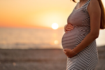 Unrecognised pregnant woman at beach on background of sea at sunset in evening.Female silhouette, mother.Happy maternity, motherhood concept.Copyspace.