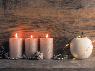 Candle of the third Advent burns, pine cones and Christmas decoration on wood