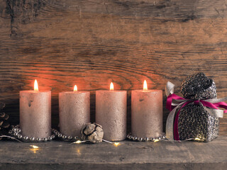 Candle of the fourth Advent burns, pine cones and Christmas decoration on wood