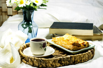 breakfast tray : Homemade puffed pastry apple tart with ice cream and daisy flowers and cup of coffee on hotel bed room with books 