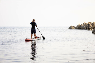 Senior man paddle surf on the beach. Male over 50 aging youthfully, paddling and doing exercise at...