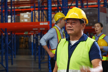 Asian male foreman wearing hard hat safety uniform Stand to inspect between the shelves that are stored inside the warehouse.