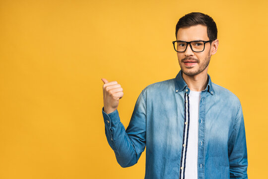 Look over there! Happy young handsome man in casual pointing away at copyspace and smiling while standing isolated over yellow background.