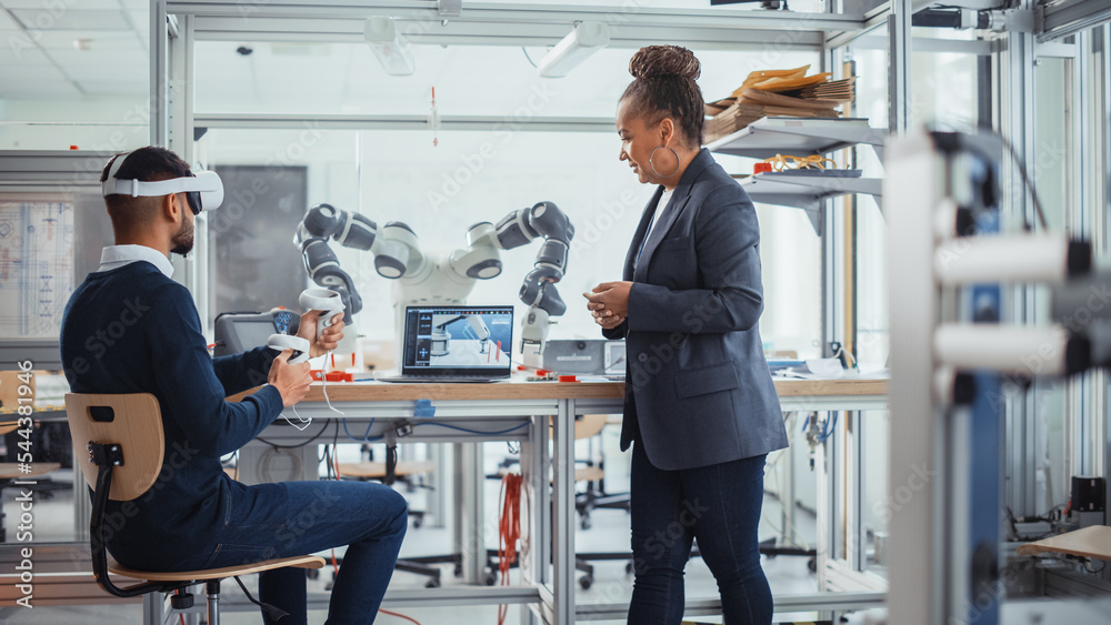 Poster Black Senior Engineer Talks to Young Male Computer Scientist Who is Wearing Virtual Reality Headset and Uses Controllers to Remotely Manipulate Robotic Hand. High Tech Research Laboratory Concept
