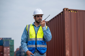Logistic Manager talking on the walkie-talkie at container warehouse for control loading containers in container yard terminal shipping, Worker container talking radio to manage the export of goods