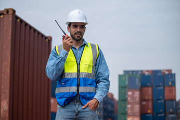 Logistic Manager talking on the walkie-talkie at container warehouse for control loading containers in container yard terminal shipping, Worker container talking radio to manage the export of goods