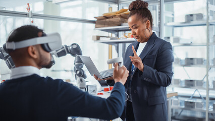 Black Senior Engineer Look at Laptop and Supervising her Young Colleague with VR Headset and Controllers. Virtual Reality Technology for Industrial Design, Development, Prototyping in CAD Software.