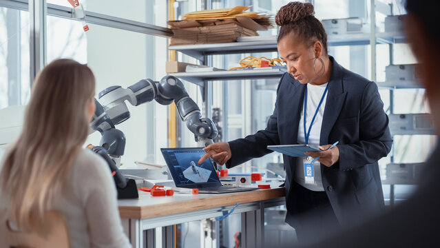 Female Computer Science Specialist Focused on Intersting Lecture by African American Professor. Diverse Group of Young Engineers Programming Robotic Hand. Advanced Robotics Class Concept.