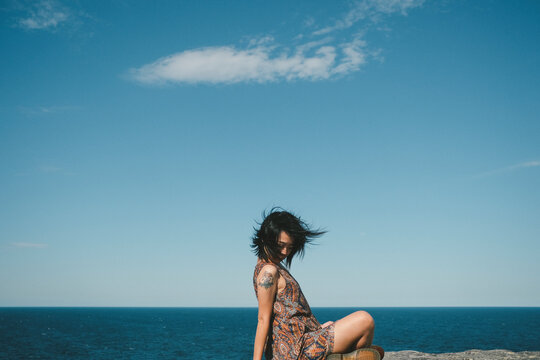 Side View Of Woman Sitting At Sea Against Sky