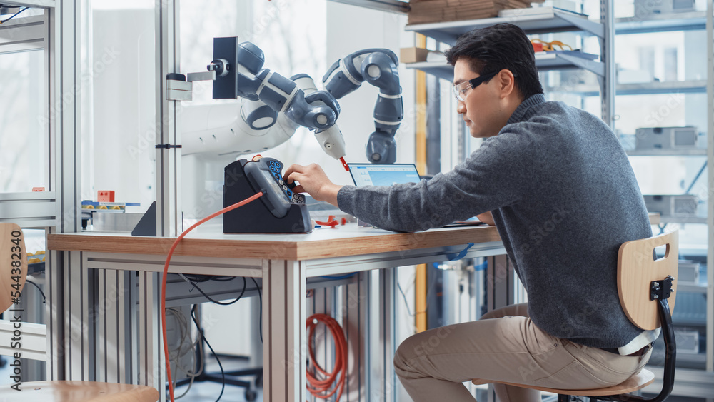 Aufkleber Asian Engineer Moving Robotic Arm with Control Panel And Developing Program on Laptop. Robotics Specialist Designs Plans and Processes Needed to Build Robots. Computer Science Laboratory.