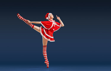 Dancing ballerina with a gift in her hands on pointe shoes in the costume of Santa Claus on a dark...