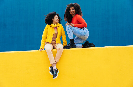 Young Female Friends Sitting On Wall